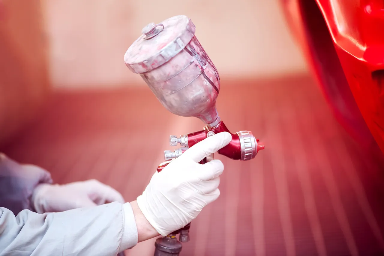Arbeiter bemalt ein rotes Auto in einer Lackierkabine